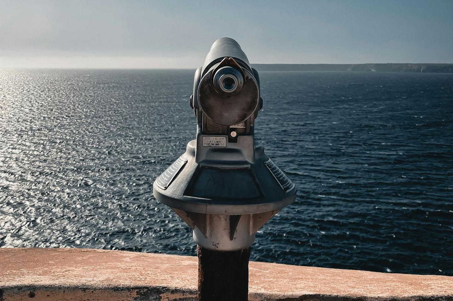 gray and black telescope on brown concrete surface near body of water during daytime